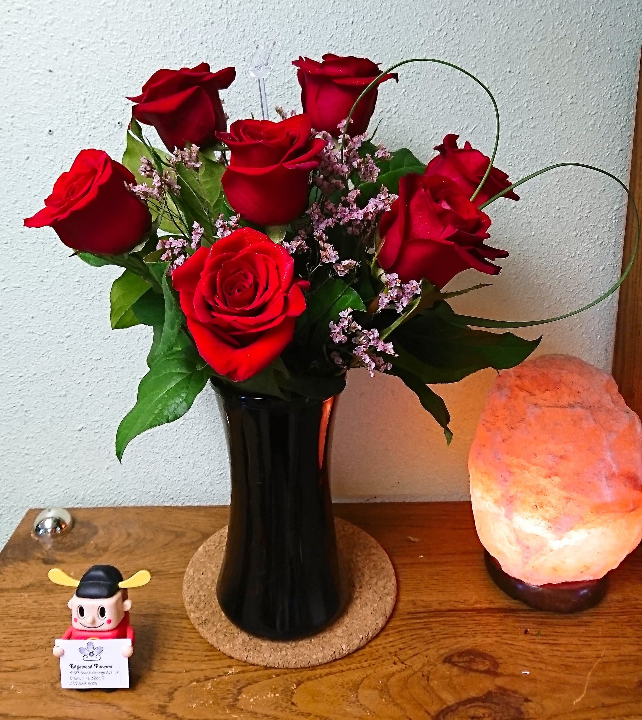 Red roses arranged in a black vase with small pink filler flowers