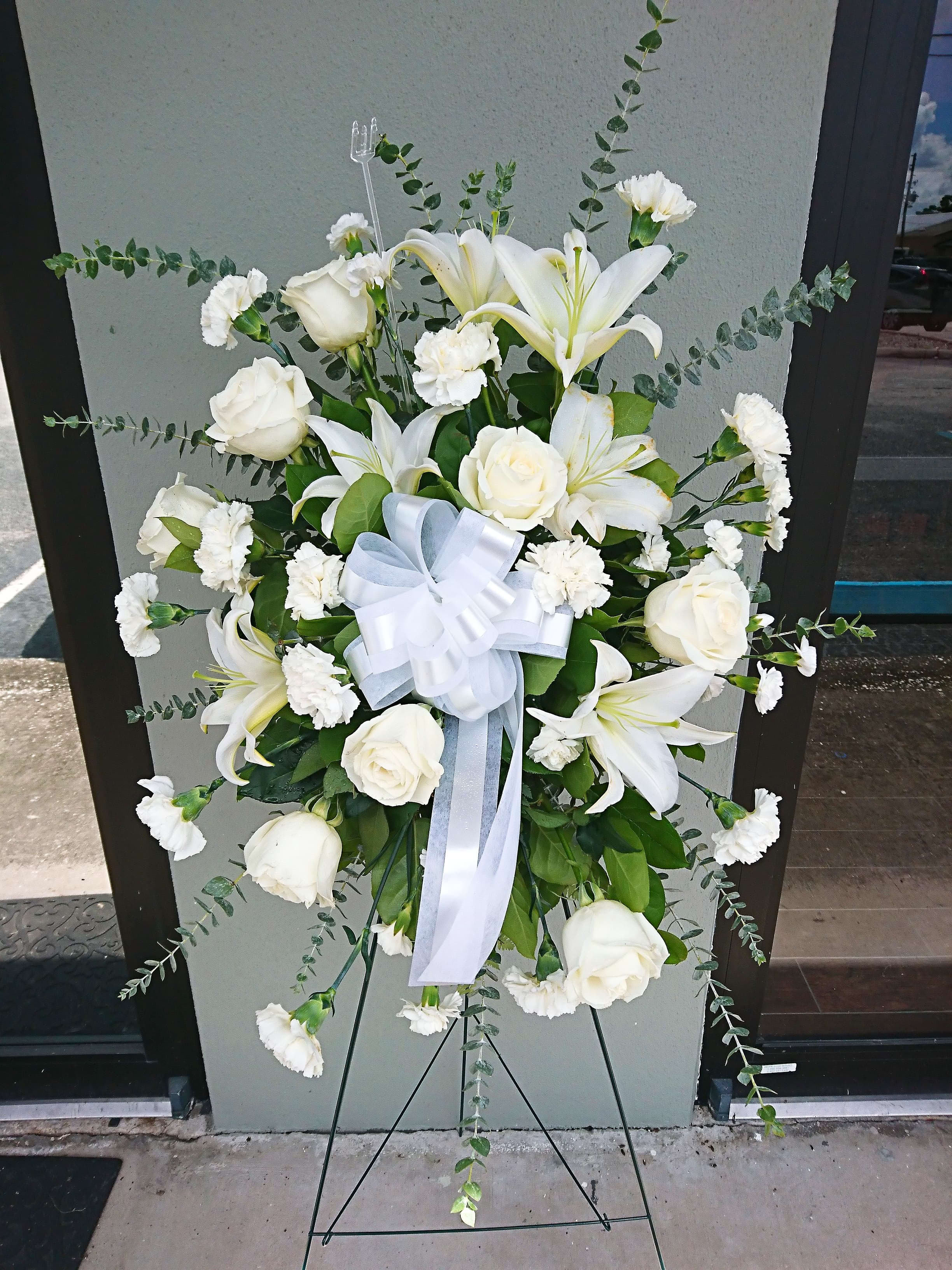White floral standing spray with roses, lilies, and carnations on an easel