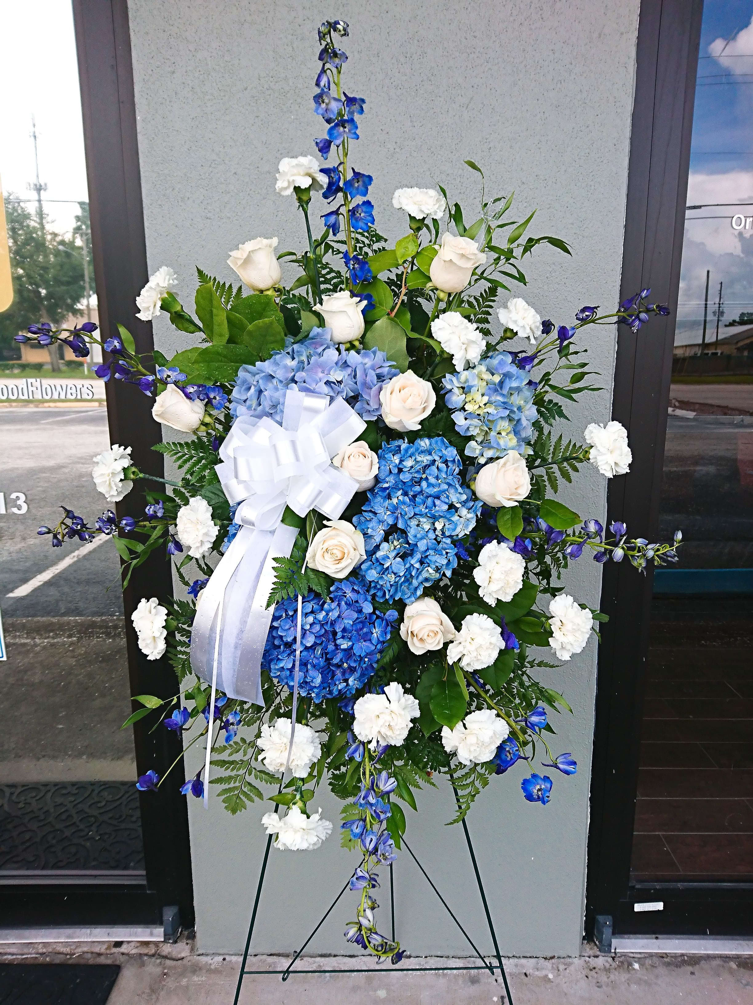Standing floral spray with blue hydrangeas, white roses, and a white ribbon