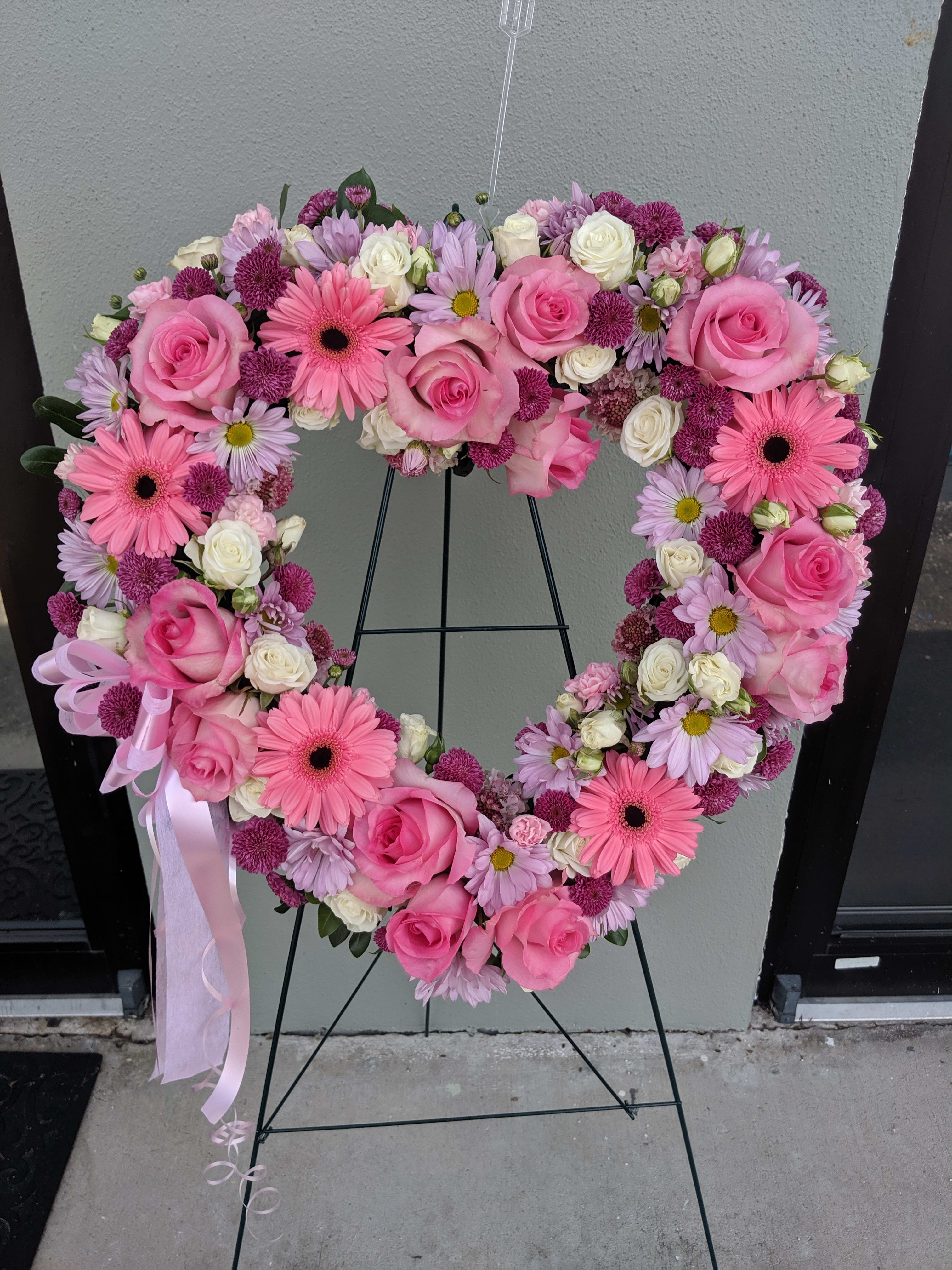 Heart-shaped floral wreath with pink roses and daisies on a stand