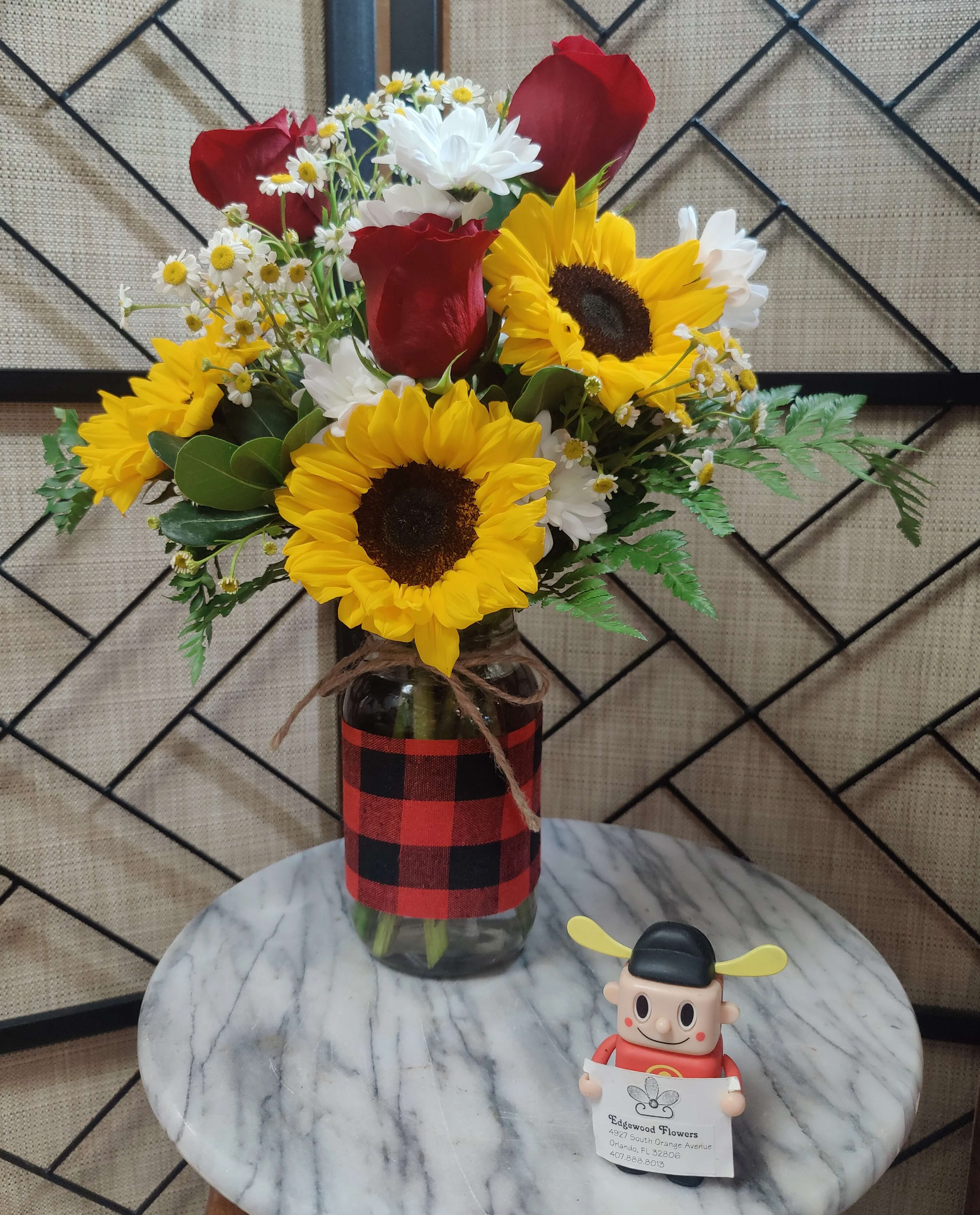 Bouquet of sunflowers, red roses, and white daisies in a glass jar
