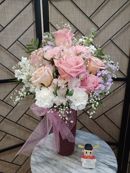 Pink and white rose bouquet in a burgundy vase with a pink ribbon