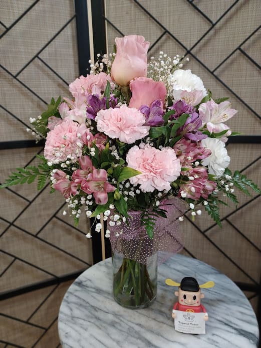 Pink and white bouquet in a glass vase with a small figurine beside it