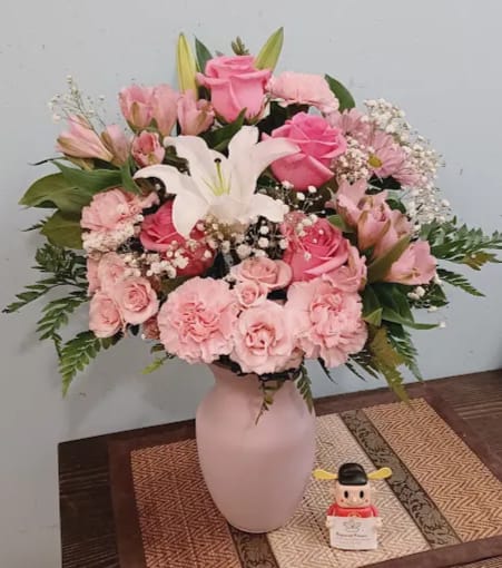 Pink and white floral arrangement in a pale vase with a small figurine beside it