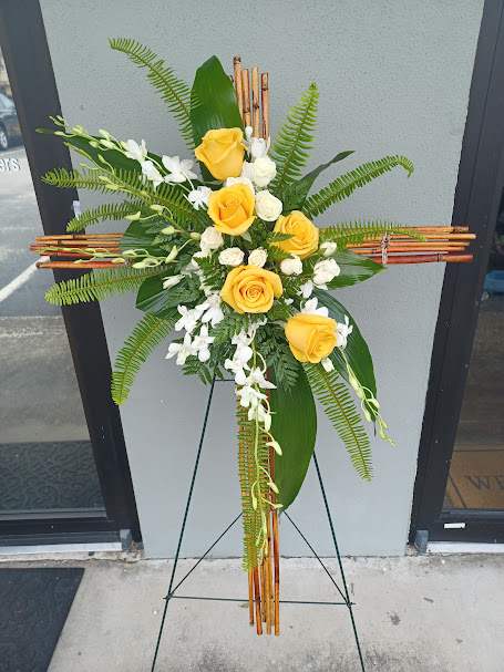 Yellow roses and white flowers arranged on a standing cross