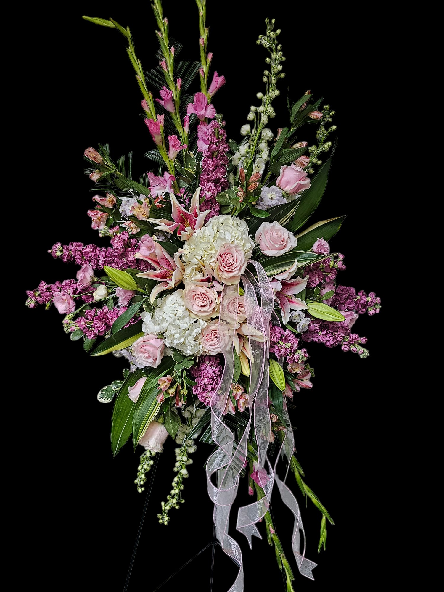 Sweet Memories Easel Spray - Soft, sweet memories of your loved one will be easy to convey with this easel spray in various shades of pink and white. Softened by sheer ribbon cascading down on one side.  This easel spray can be ordered as it is shown, or in the colors of your choice, depending on availability, some of the flowers may be different, but the same feeling will be portrayed.