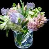 Soft Spring - Soft pink hyacinths and airy lavender blooms combine with creamy white stock and sweet pea for a gentle, springtime bouquet-perfect as a Mother's Day arrangement, a birthday bouquet, or a comforting get-well or sympathy gift. The relaxed, garden-inspired shape leans slightly to one side, giving the person you're thinking of a feeling of effortless charm and calm the moment it arrives.  Arranged in a short clear glass vase and set in water, this pastel mix highlights soft textures and subtle fragrance: the clustered hyacinth heads, delicate stock petals, and fluttery sweet pea stems create a layered, tactile look that reads fresh and intimate. The compact size makes it right for a bedside table, mantel, or small dining table where its tender palette can be appreciated up close.  Choose this bouquet when you want to make someone feel gently cared for-whether celebrating spring, offering sympathy, or brightening a recovery. Vase-ready and easy to place, it arrives arranged and hydrated for immediate enjoyment; regular fresh water and a cool spot will keep the blooms looking their best.