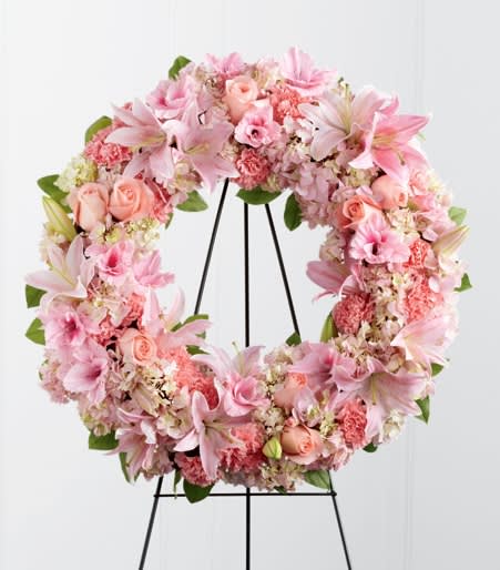 Pink floral wreath on a black stand with lilies and roses