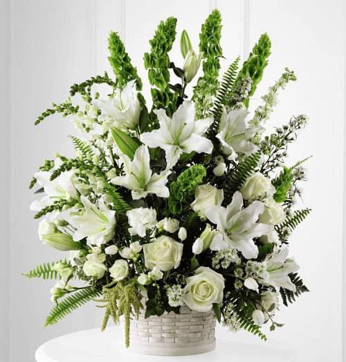 White lilies and roses arranged in a white basket with green accents
