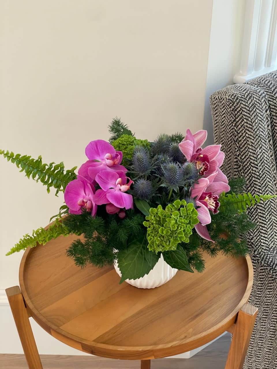 Pink orchids and blue thistle in a white vase