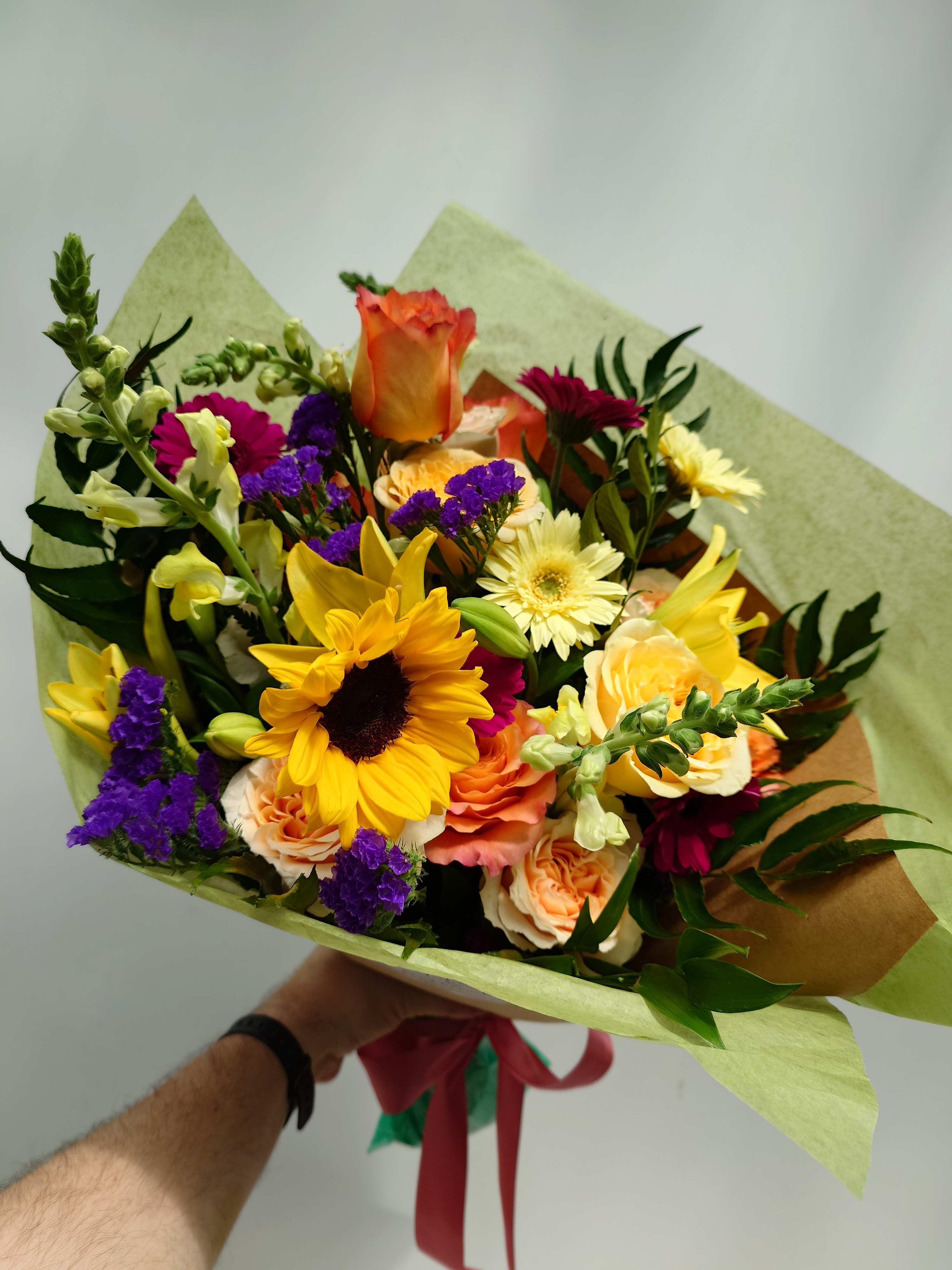 Mixed bouquet with sunflowers, roses, and purple filler flowers wrapped in paper