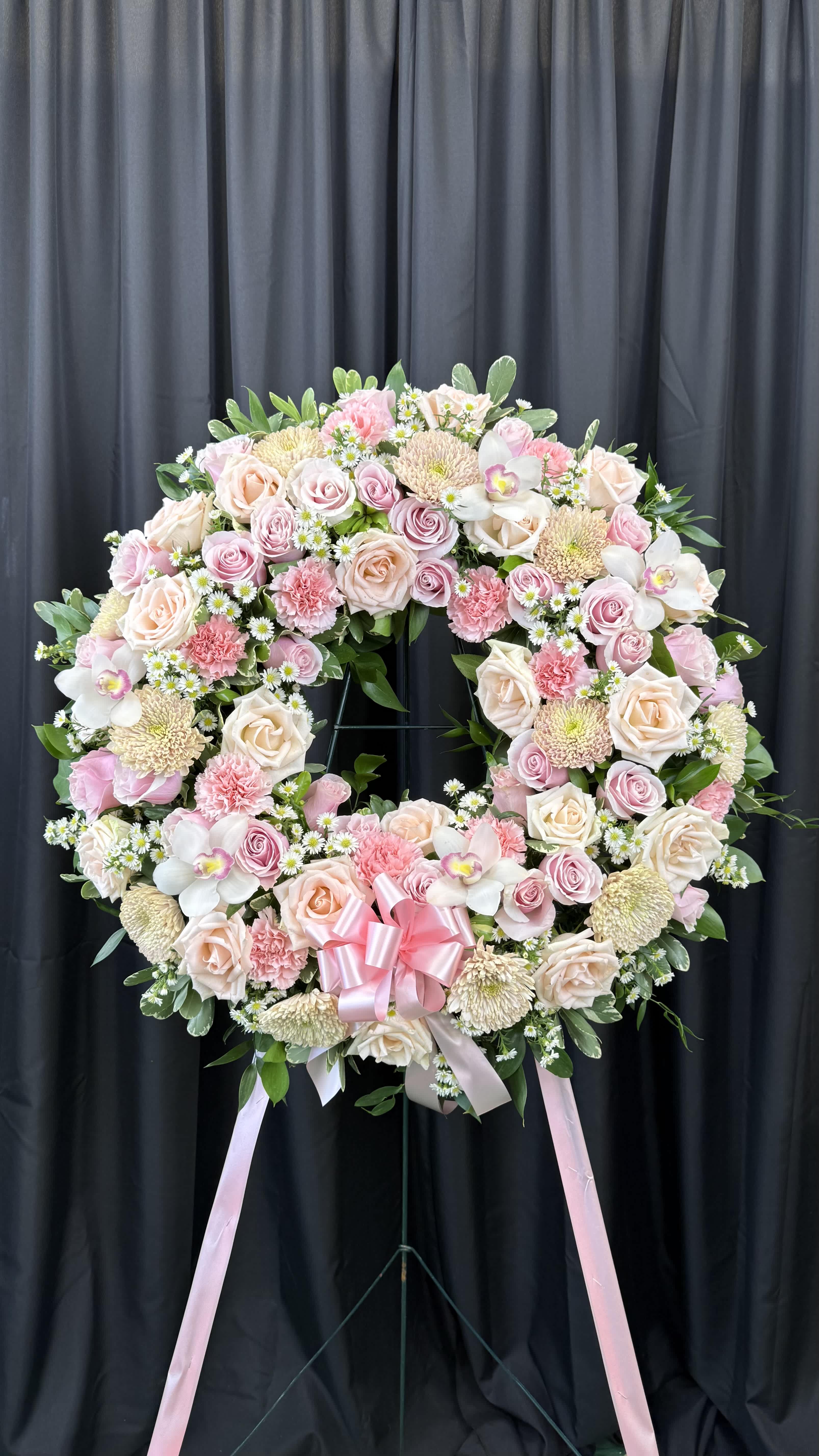 Large pink and cream floral wreath on a stand with a pink ribbon bow