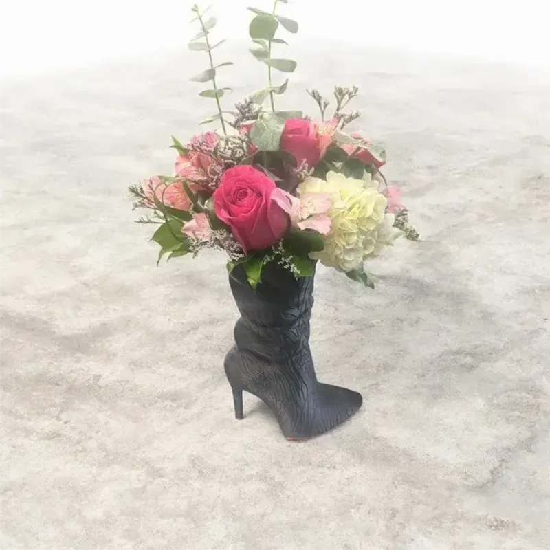 Mom's Diva Boot - A bright pink rose takes center stage in this fashion-forward flower arrangement, set playfully inside a black high-heel boot vase-perfect as a birthday bouquet or a whimsical "thinking of you" gift. The pink, green, white and black palette reads feminine and fun, making it an ideal choice for graduations, thank-you gestures, or a just-because surprise that will make the person you're thinking of feel seen and celebrated.  Creamy white hydrangea clusters, pale pink blooms, alstroemeria and additional roses form a compact, rounded bouquet at the foot of the boot, while tall eucalyptus stems add vertical movement and a hint of silvery green above the blooms. The black boot vase doubles as a decorative keepsake, bringing personality to bedside tables or desks. This arrangement arrives ready to display-no extra styling needed-and is a cheerful, slightly whimsical way to mark Mother's Day or any casual occasion year-round.
