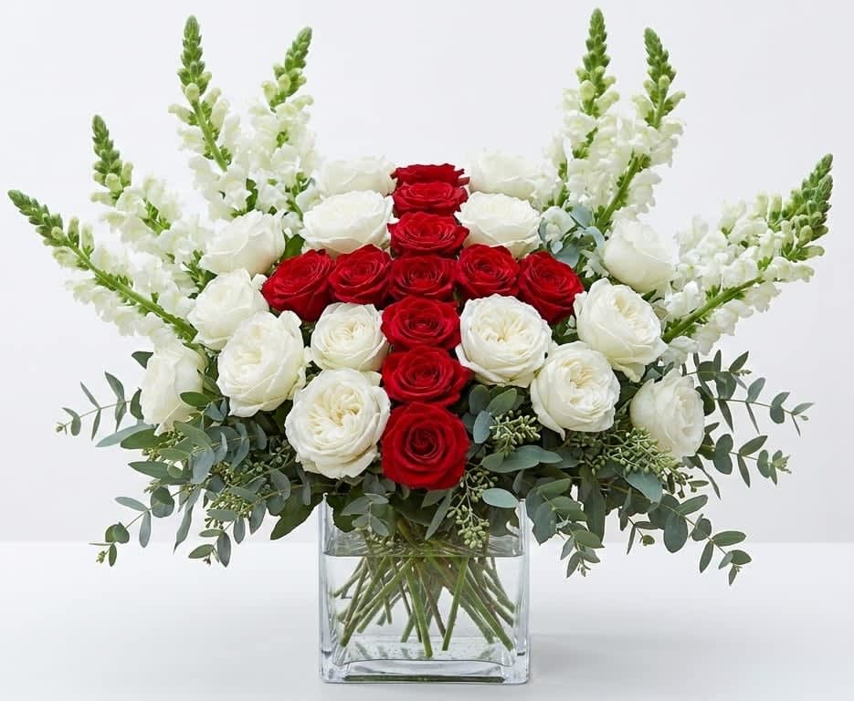 The Three Lions - England - A bold cluster of red and white roses creates an unmistakable, patriotic centerpiece-perfect for a FIFA World Cup collection and for cheering on the England soccer team. This upright flower arrangement reads as both celebratory and elegant, making it a great choice for game-day gifts, fan rooms, or sending to the person you want to rally with: they'll feel seen and spirited the moment this arrives.  Carefully curated roses sit tightly together in a clear square glass vase while tall white snapdragons rise at the sides and back to give the design height and a formal, balanced silhouette. Muted eucalyptus foliage at the base softens the red-and-white contrast and adds a fresh, classic texture; the palette of red, white, and green keeps the look crisp and visually striking. The vase's clean lines showcase the stems and make the arrangement easy to place on tabletops or mantels.  Whether you're celebrating a match, marking a victory, or sending encouragement during tournament season, this polished arrangement reads as thoughtful and luxe. Designed for easy display and lasting impact, it's ready to present as a fan-forward gift; follow basic care by keeping water fresh and trimming stems if you need to refresh the display.