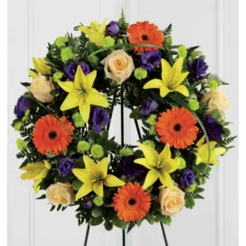 FTD® Radiance Remembrance Wreath™ - Yellow lillies and button poms are elaborately arranged to form a special wreath accented with bright orange gerber daisies and sweet peach roses to create a beautiful tribute offering peace and tranquility to those attending the final farewell service. Displayed on a wire easel. 