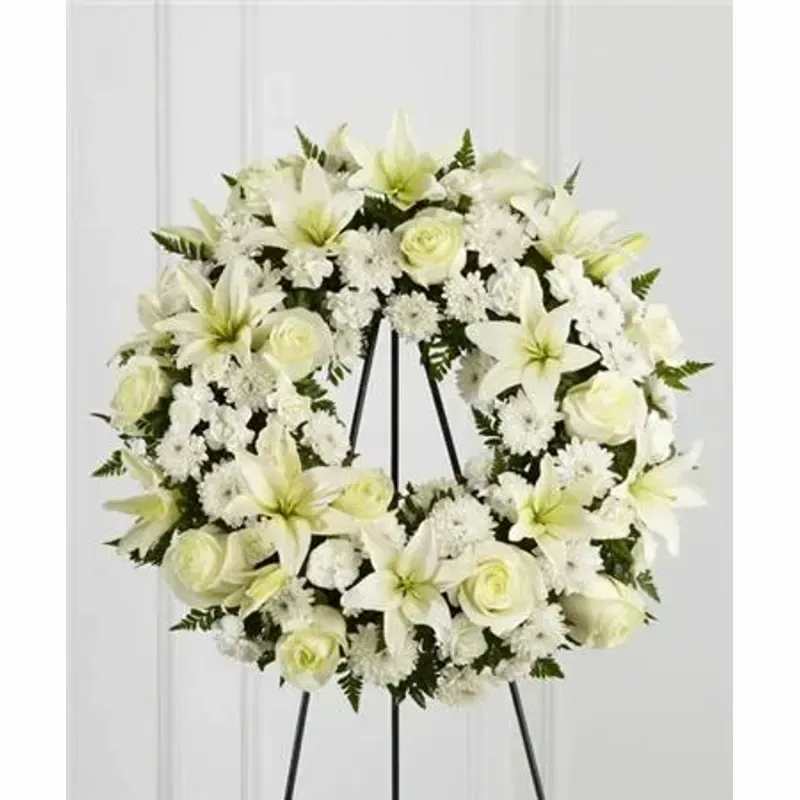 FTD Treasured Tribute™ Wreath - Bright white roses, Asiatic lilies, mini carnations and cushion poms are beautifully arranged to form an elegant accented with lush and vibrant greens. Displayed on a wire easel, this gorgeous tribute is a wonderful symbol of eternal life and sweet serenity. Approximately 22 inches in diameter. 