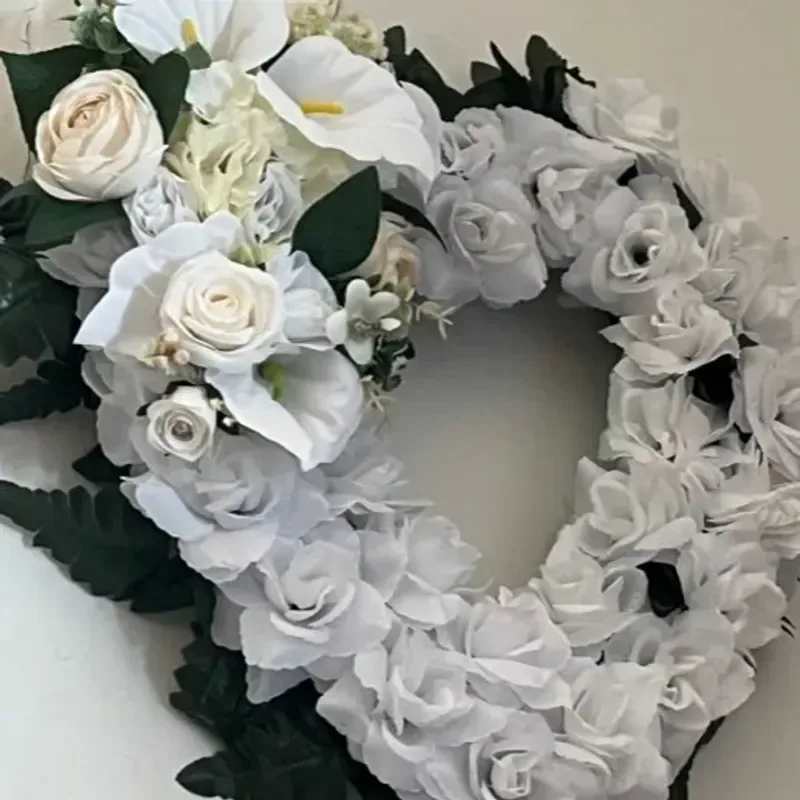 Memorial Wreath X20 - A heart-shaped wreath of densely clustered white roses and graceful white calla lilies creates a quiet, reverent statement for sympathy and funeral services. This memorial wreath is designed to convey sincere remembrance-the person you're honoring will be met with a soft, elegant tribute that feels both romantic and respectful.  Pale gray‑white filler blooms add subtle texture among the roses and calla lilies while deep green foliage frames the outer edge, giving the arrangement crisp contrast and a formal silhouette. The monochrome palette and compact, heart-shaped design make the piece visually cohesive and appropriate for chapel display, graveside service, or a remembrance table.  Comforting and understated, this wreath suits families seeking a dignified way to say goodbye or to mark a quiet anniversary of loss. Size and handling details follow standard memorial delivery protocols; please contact us with service time and placement instructions so we can ensure timely, respectful delivery.