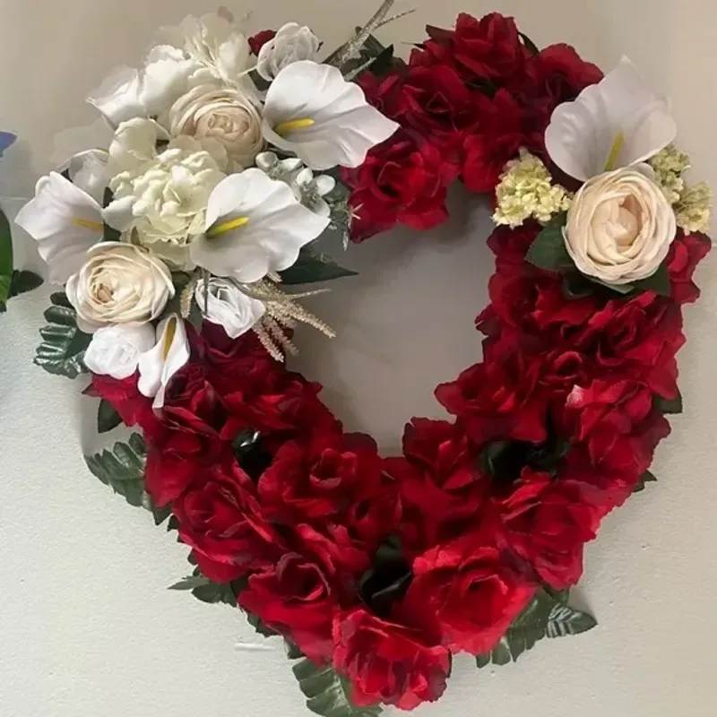 Memorial Wreath x9 - A heart-shaped wreath rendered in deep reds and pristine whites, this sympathy floral arrangement speaks of love and remembrance with quiet elegance - perfect for a funeral or memorial service. The heart form and rich red blooms convey a message of lasting affection, while the white accents offer peace and comfort to the person you're honoring.  Dense clusters of red carnations and other red blooms form the wreath's bold outline, while white calla lilies and cream rose-like flowers create luminous focal points against dark green foliage. The symmetrical design is crafted for visual impact from a distance and close-up texture, combining soft petals and glossy leaves for a refined, ceremonial presentation.  Made to sit respectfully at a service or graveside, this wreath is an expressive tribute that will help the bereaved feel remembered and loved. Size and delivery details are handled at checkout; arrange for funeral home delivery or pick a preferred date to ensure it arrives for the ceremony.