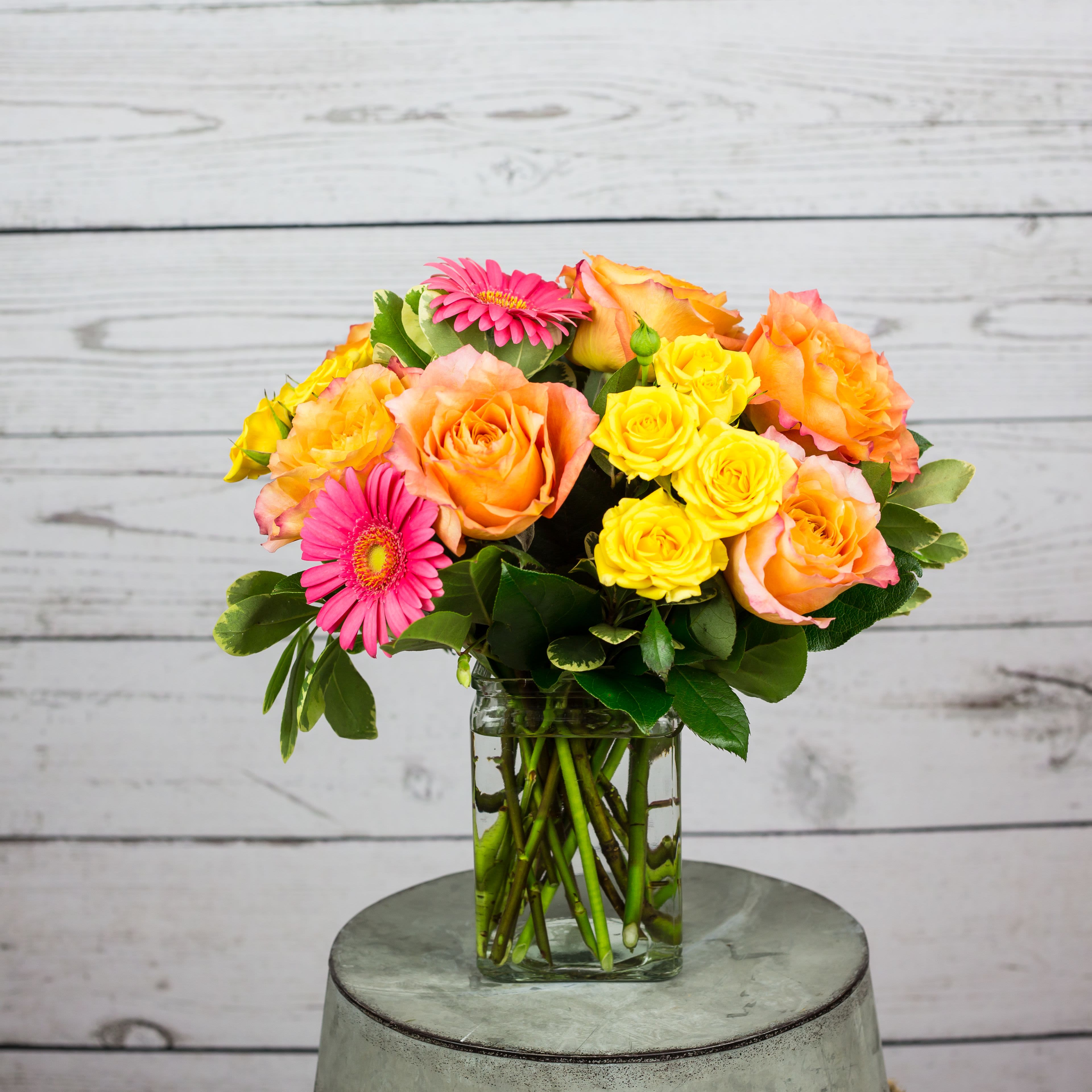 Bouquet of orange and yellow roses with pink gerbera daisies in a glass vase