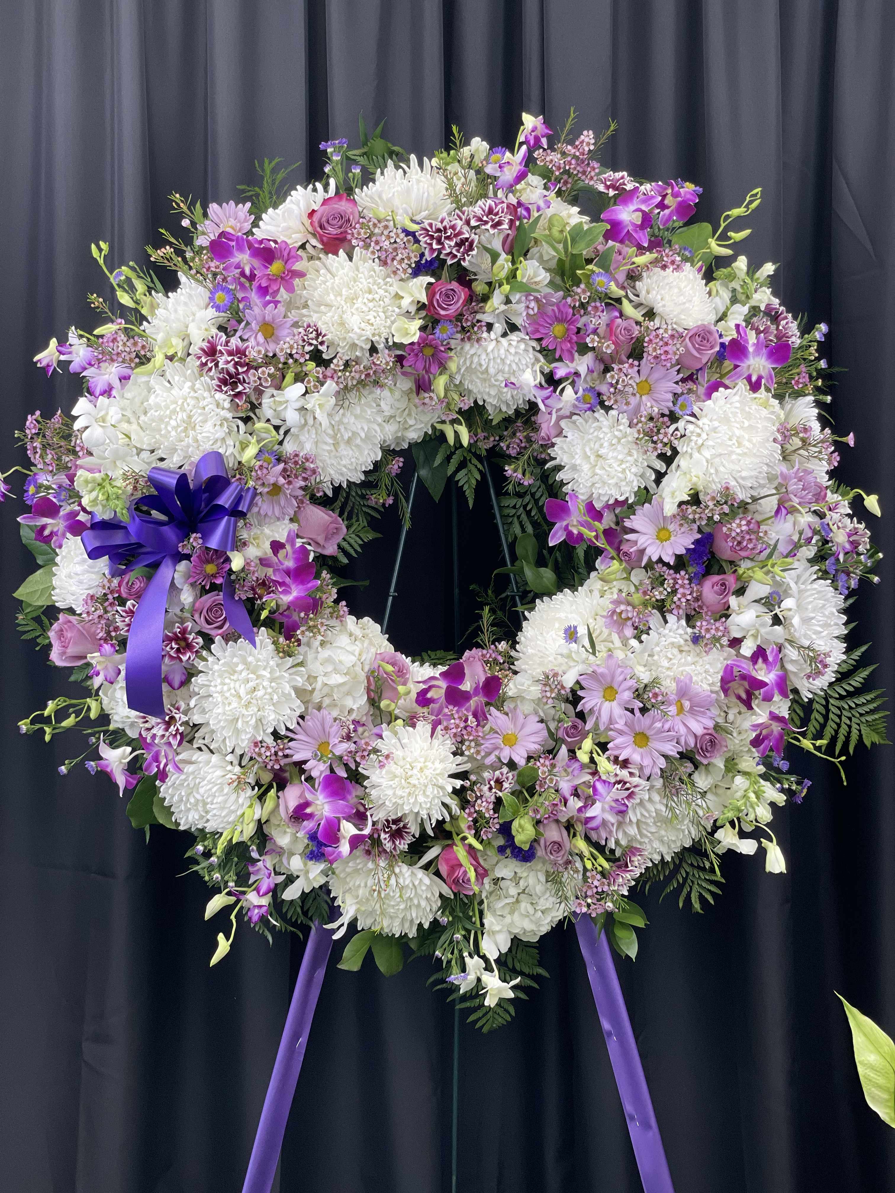Large purple and white floral wreath on a stand with a ribbon bow
