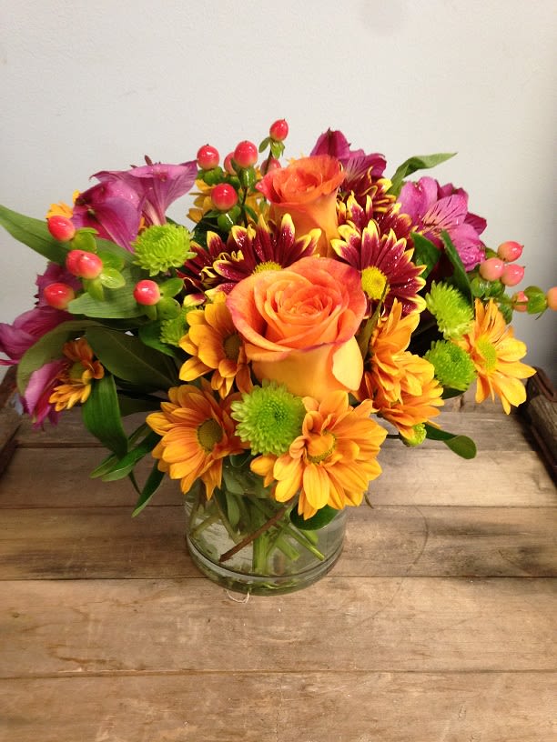 Mixed bouquet of orange roses, daisies, and purple flowers in a glass vase