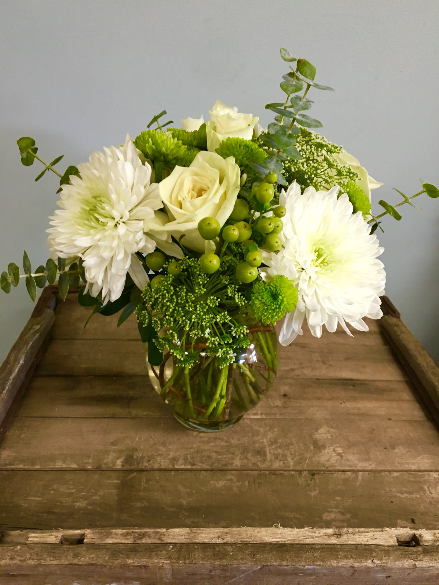 White roses and chrysanthemums in a glass vase with green accents