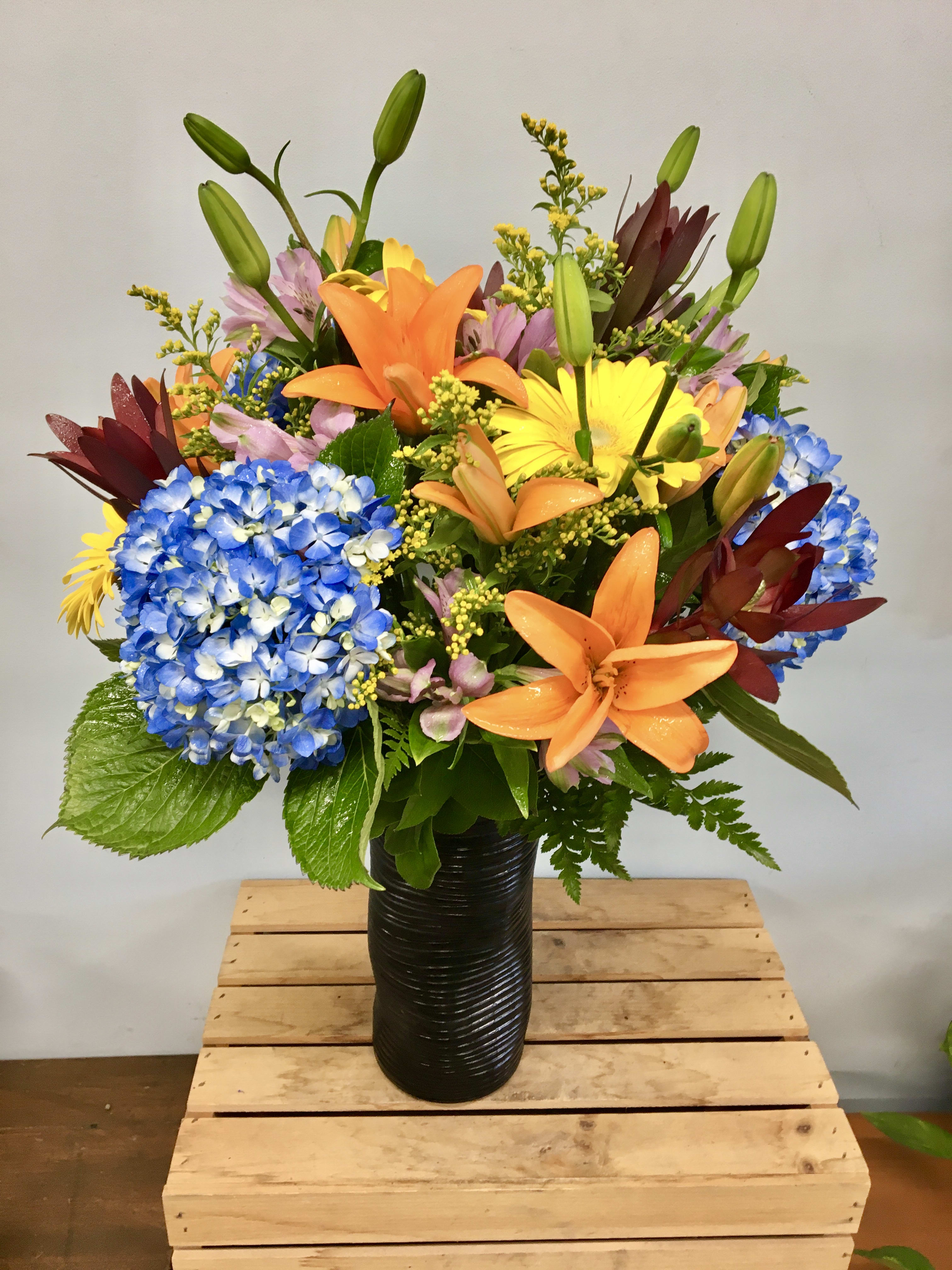 Colorful bouquet with lilies, hydrangeas, and gerbera daisies in a black vase