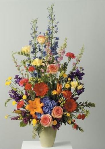Tall mixed bouquet in a pale vase with roses, lilies, and blue flowers
