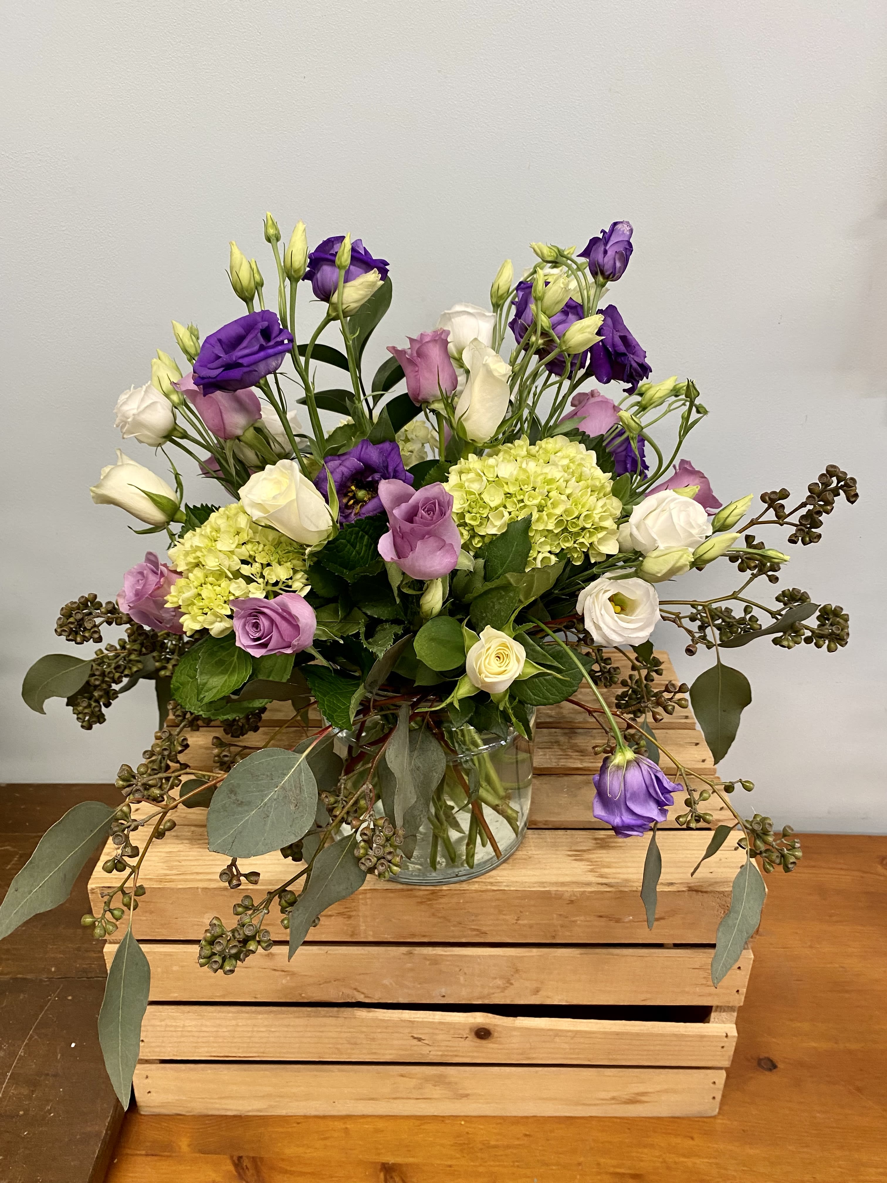 Purple and white flowers in a glass vase with trailing greenery
