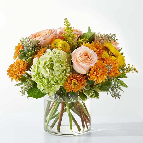 Peach roses and orange mums in a clear glass vase