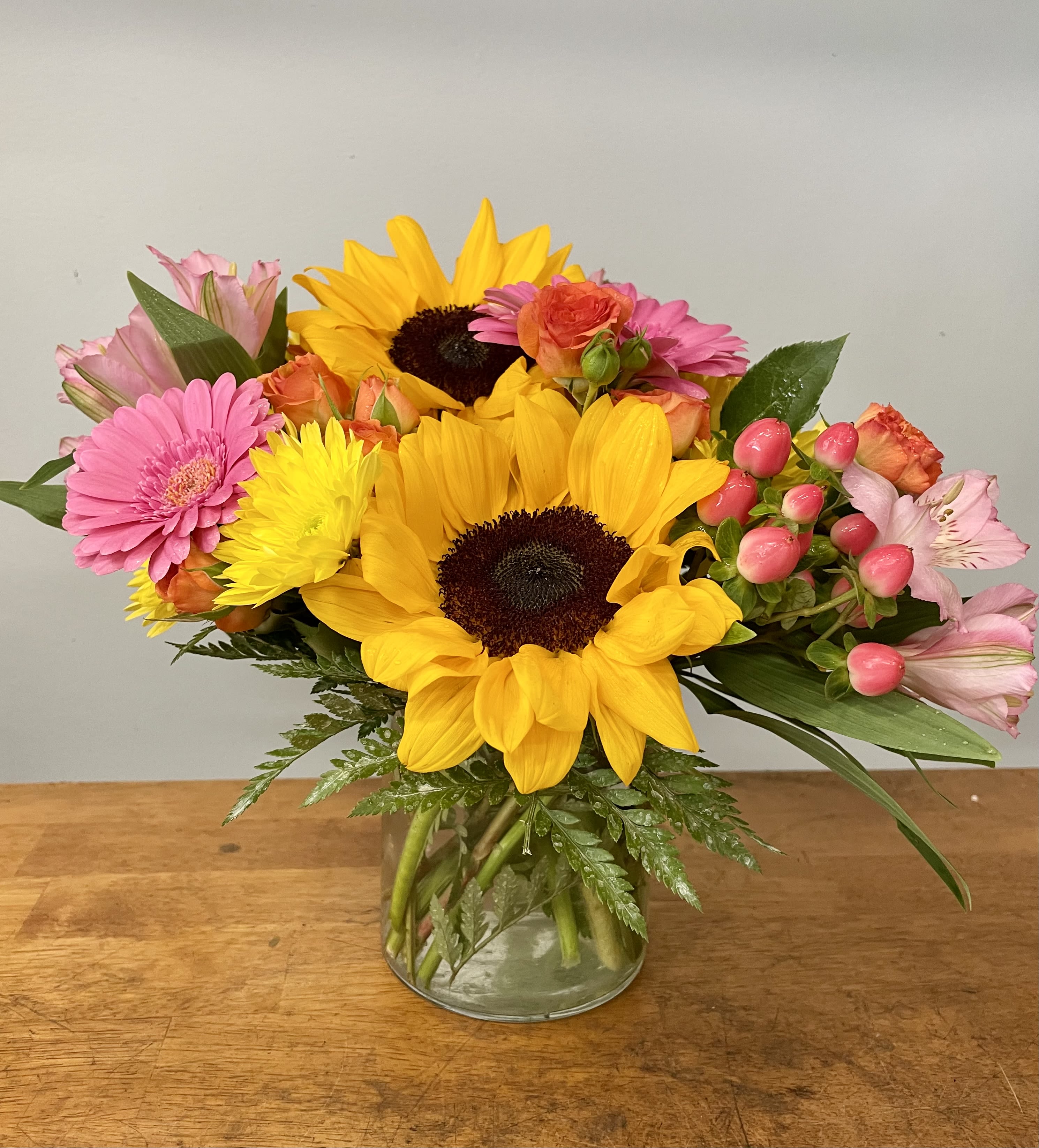 Mixed bouquet with sunflowers, pink gerberas, and roses in a glass vase