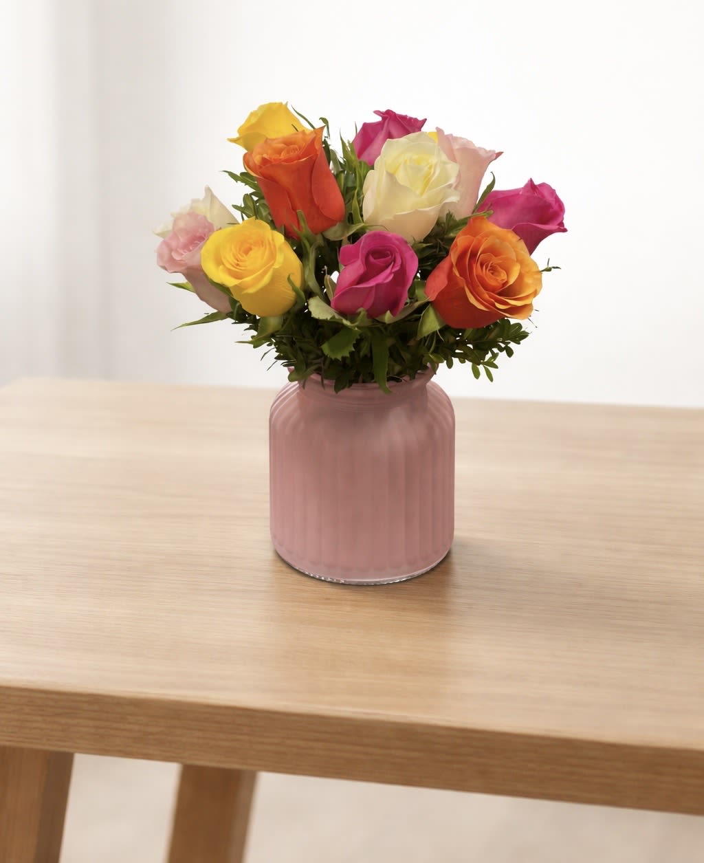 Mixed roses in a pink glass vase on a wooden table