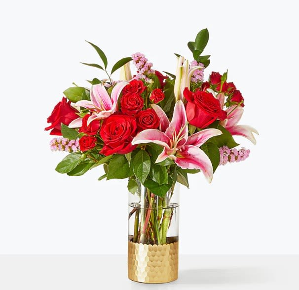 Red roses and pink lilies arranged in a glass vase with a gold base.