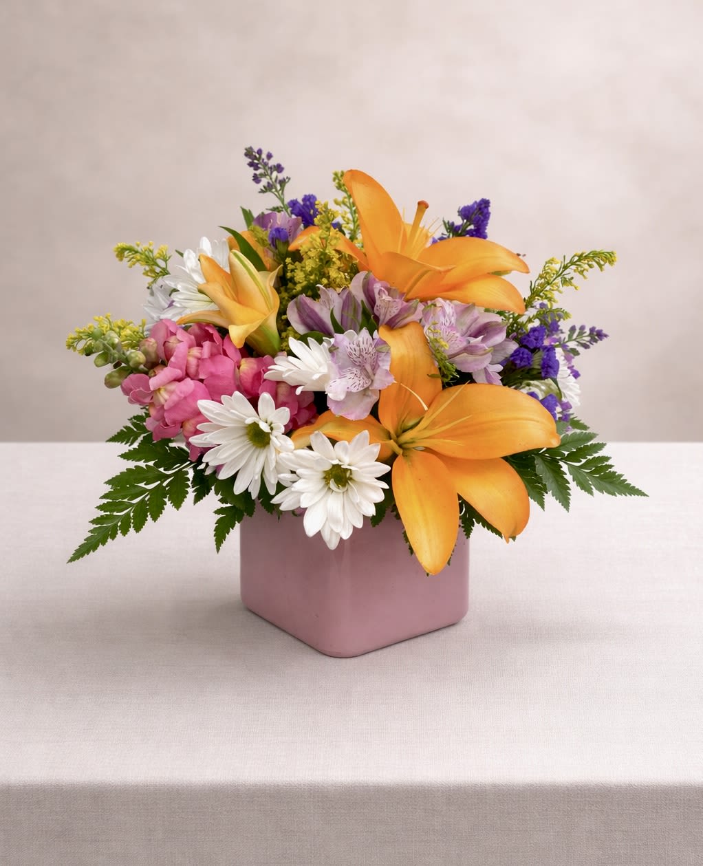 Mixed bouquet of orange lilies, pink flowers, and white daisies in a pink vase