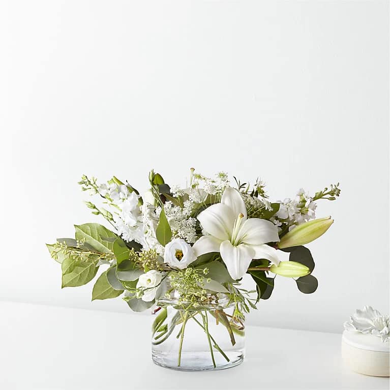 White lilies and small white blooms in a clear glass vase