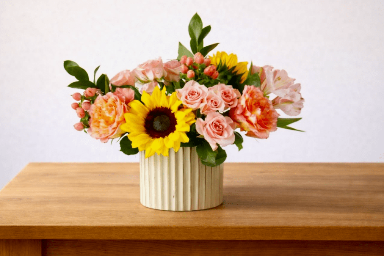 Mixed bouquet with sunflowers, pink roses, and carnations in a ribbed vase