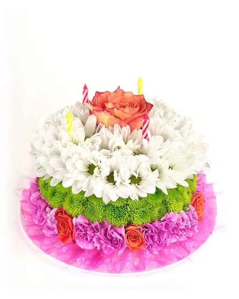 HAPPY FLOWER CAKE - The slice of happiness! This birthday cake bouquet of Roses, mini carnations and poms is great selection on their special day. This cake arrangement is made up of orange roses, pink miniature carnations, green button pom and white Daisy pom. Delivered on a designer tray.