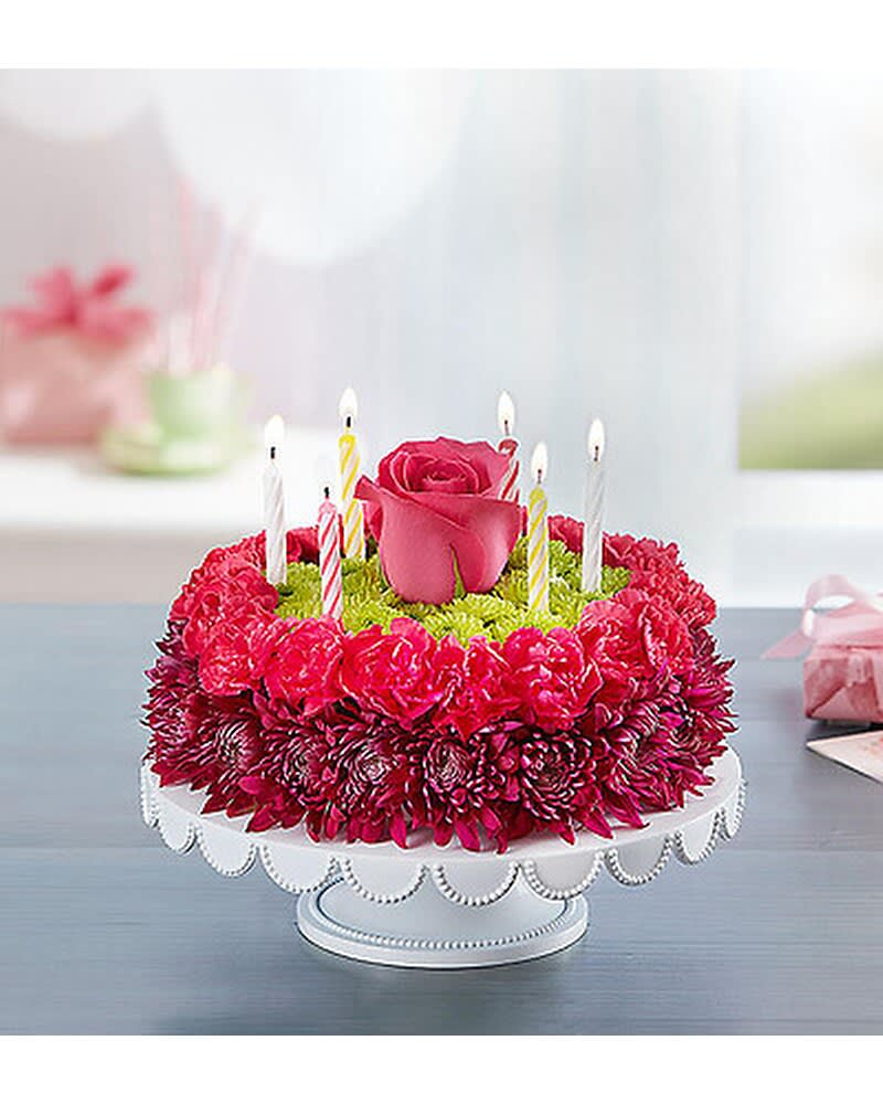 BIRTHDAY WISHES FLOWER CAKE - PURPLE - Purple adds a happy pop with this Birthday Wishes Flower Cake. Handcrafted with fresh carnations, mums, and poms in shades of purple, pink, and green, it’s a unique and festive centerpiece for a memorable celebration. Want to make the day even more special? A birthday balloon will take the fun to new heights!  *****VASE PLATE WILL VARY ******