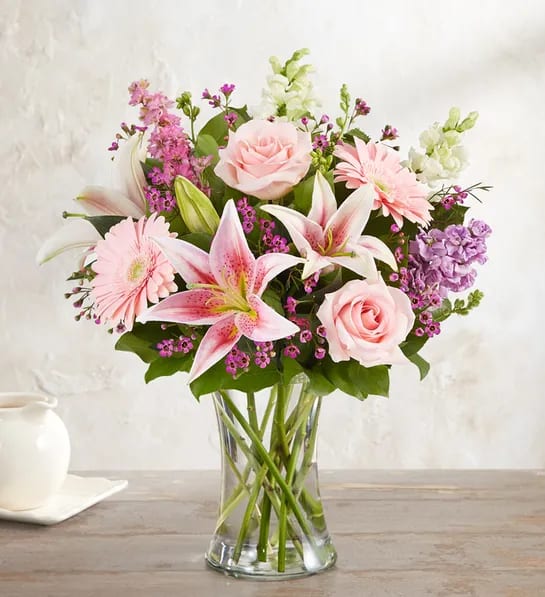 Pink roses, lilies, and gerbera daisies in a clear glass vase