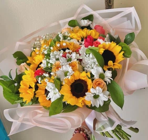 Springful Wrapped Bouquet - Bouquet of Sunflowers, Roses, Mini Roses, White Daises, and Ruscus, with baby breath accents. Paper and Flower color may vary depending on availability. 