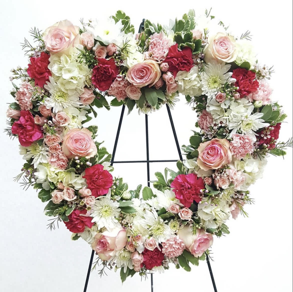 Pinks and White Funeral Heart - The use of color in a sympathy tribute can evoke emotions that words otherwise can’t. In our Pinks and White Funeral Heart, a gorgeous display of bold pinks and comforting whites come together in a timeless expression of sympathy. This arrangement comes expertly crafted by our local florists with stock, roses and carnations to show how much you care.