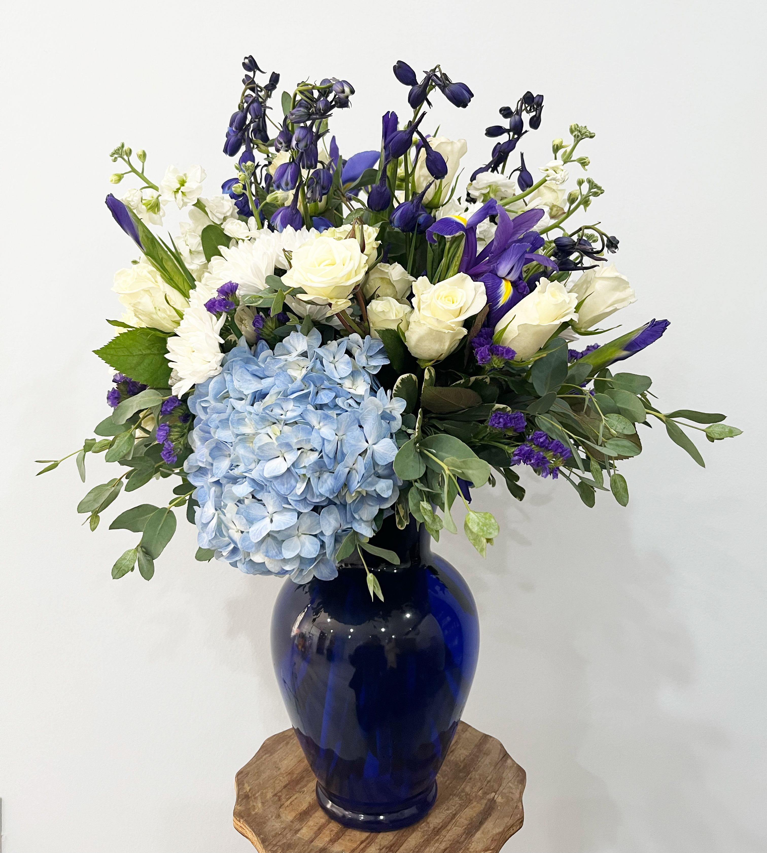 Royal Elegance Bouquet - Elevate any space with the timeless beauty of our Royal Elegance Bouquet, an exquisite arrangement of fresh blooms in soft blues, deep purples, and creamy whites. Featuring lush hydrangeas, delicate roses, irises, and seasonal wildflowers, this bouquet is artfully designed in a striking cobalt blue vase. Perfect for celebrations, sympathy gestures, or simply bringing a touch of refined beauty to any home or office. Let the serene hues and lush textures of this arrangement convey your heartfelt emotions with grace and sophistication.
