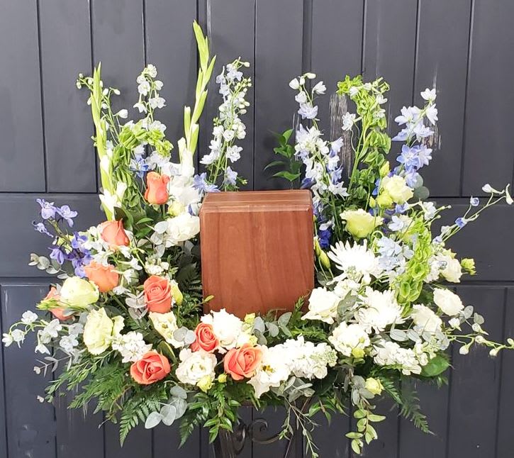 Heavenly Garden Memorial Cremation Tribute - Honor a beautiful life with our "Heavenly Garden Memorial Cremation Tribute" This stunning arrangement of soft peach roses, creamy white blooms, delicate blue delphiniums, and lush greenery is designed to lovingly cradle an urn in a vibrant display of remembrance and peace. Thoughtfully handcrafted with fresh seasonal flowers, this tribute brings comfort and grace to any memorial service. Flowers and colors may vary slightly based on seasonal availability, ensuring each arrangement is uniquely special.