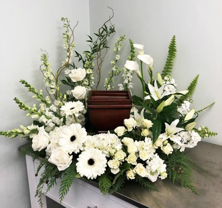 Pure Grace Surround Cremation Tribute - Celebrate a life filled with love and light with our "Pure Grace Surround Cremation Tribute" This stunning arrangement of elegant white roses, lilies, calla lilies, gerbera daisies, and lush greenery is thoughtfully designed to create a peaceful, heavenly tribute around your loved one’s urn. The pure white palette symbolizes eternal love, remembrance, and serenity, offering a beautiful expression of sympathy during times of loss. Flower varieties and greenery may vary slightly depending on seasonal availability.