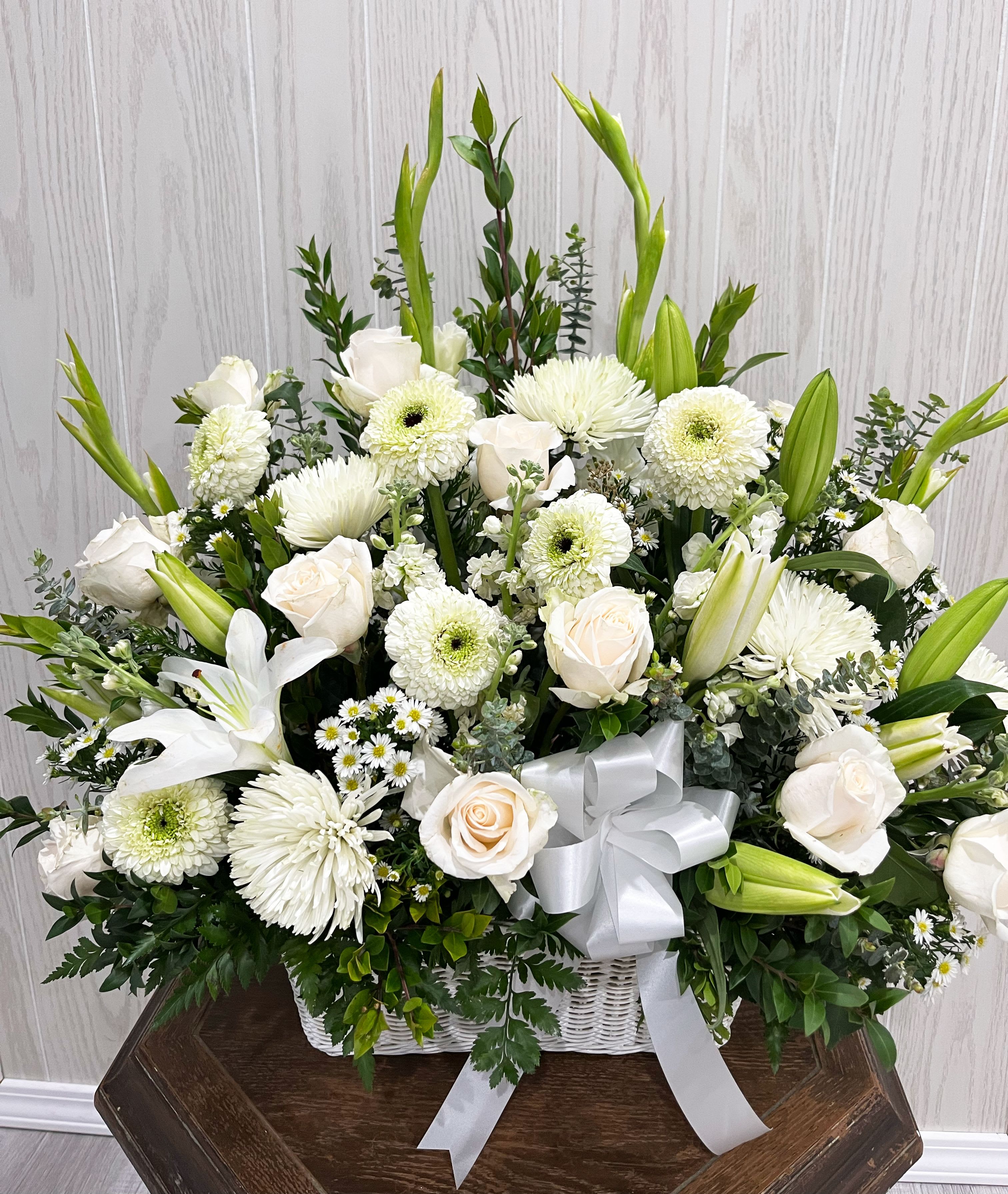 White Sympathy Basket - Our White Sympathy Basket is a beautiful symbol of love. Pure white flowers are artistically arranged in a lovely basket to create a simple but elegant display. It is a special way to extend your sympathy and support.  Item pictured is a depiction of an arrangement that we will make as similar as possible with the same look and feel.