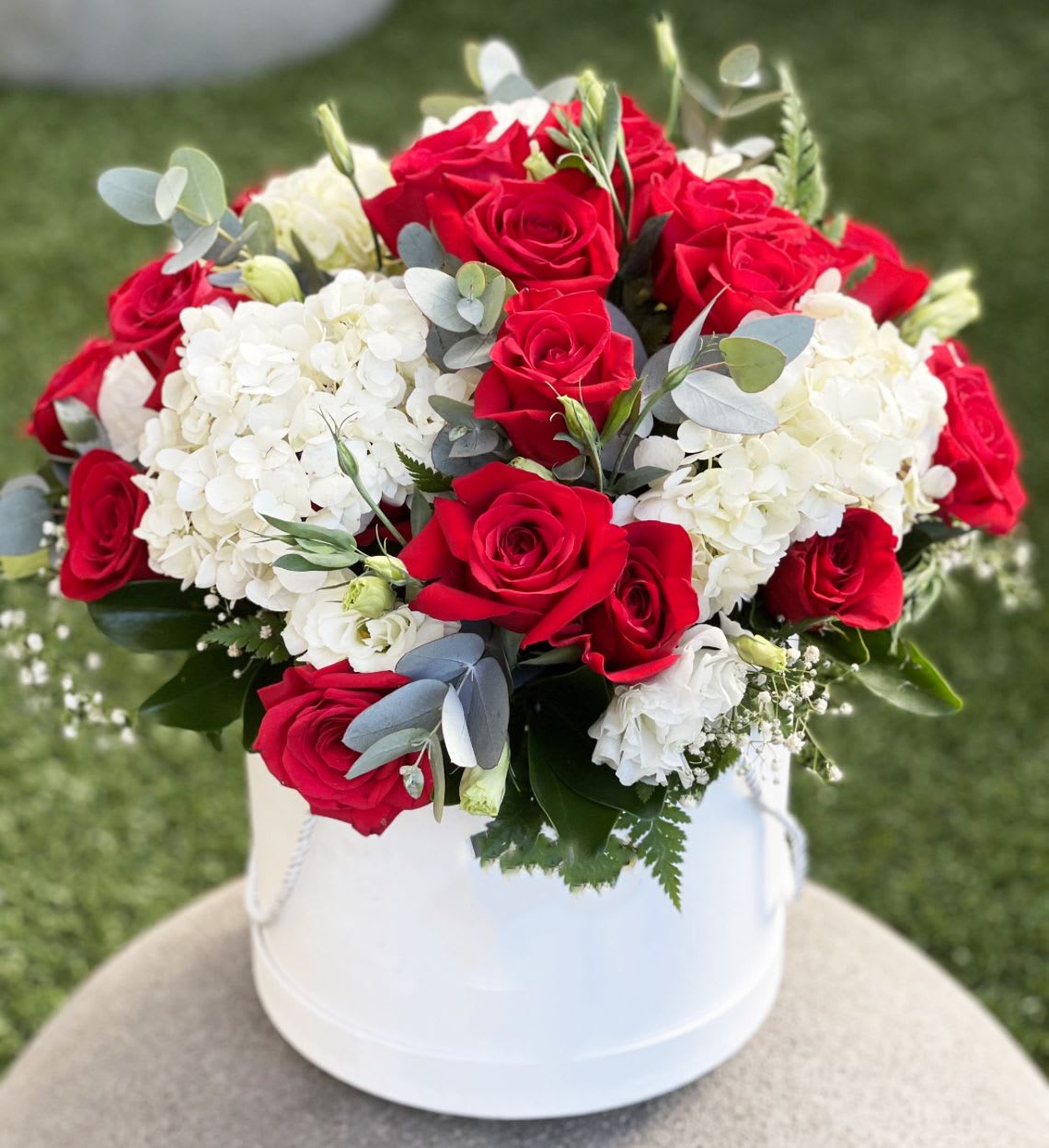 Romance &amp; Grace Bloom Box - Elegance meets passion in this luxurious floral arrangement featuring bold red roses paired with lush white hydrangeas, soft lisianthus, eucalyptus accents, and delicate baby’s breath. Expertly arranged in a sleek white hatbox, this timeless design is perfect for anniversaries, romantic gestures, or elegant gifting.