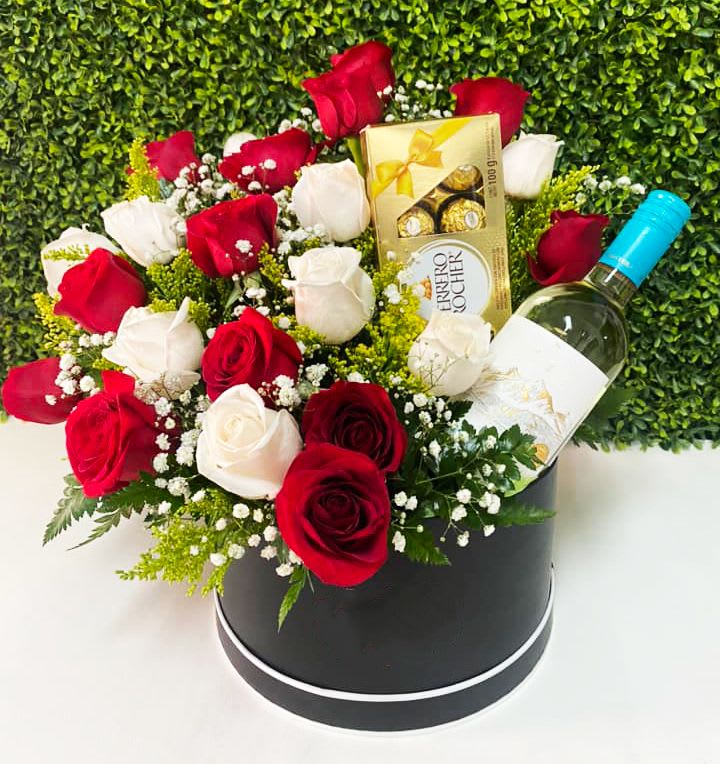 Red and white roses arranged in a black hat box with wine and chocolates