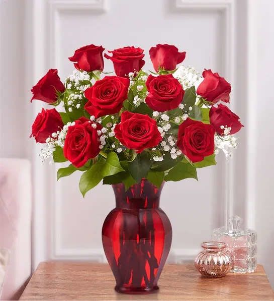 Red roses arranged in a red glass vase with white filler flowers
