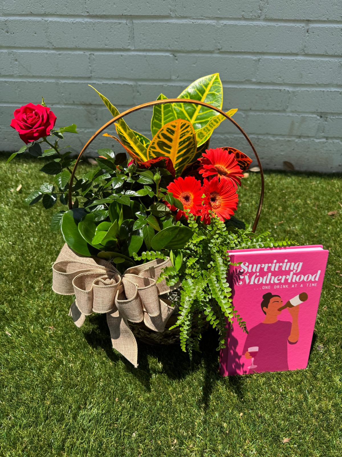 Basket arrangement with a red rose, orange gerberas, and a pink card