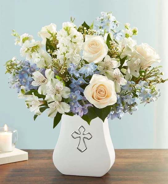 White and pale blue flower arrangement in a white vase with a cross emblem
